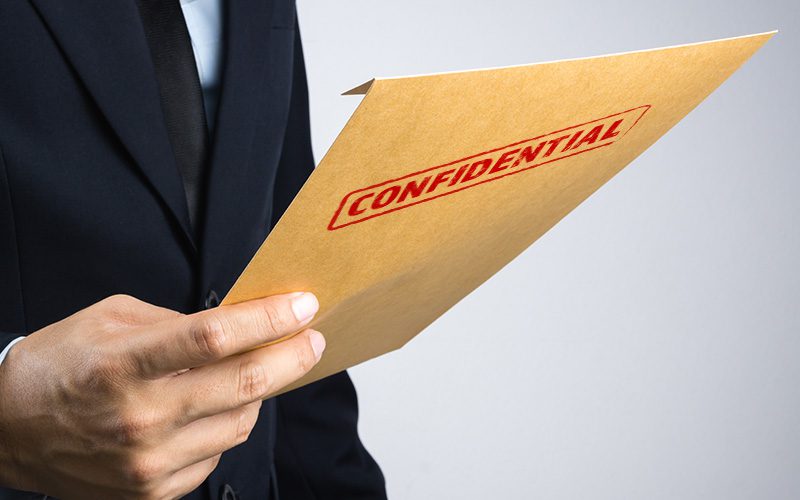 Close up of a man holding a confidential manila envelope in his hand.